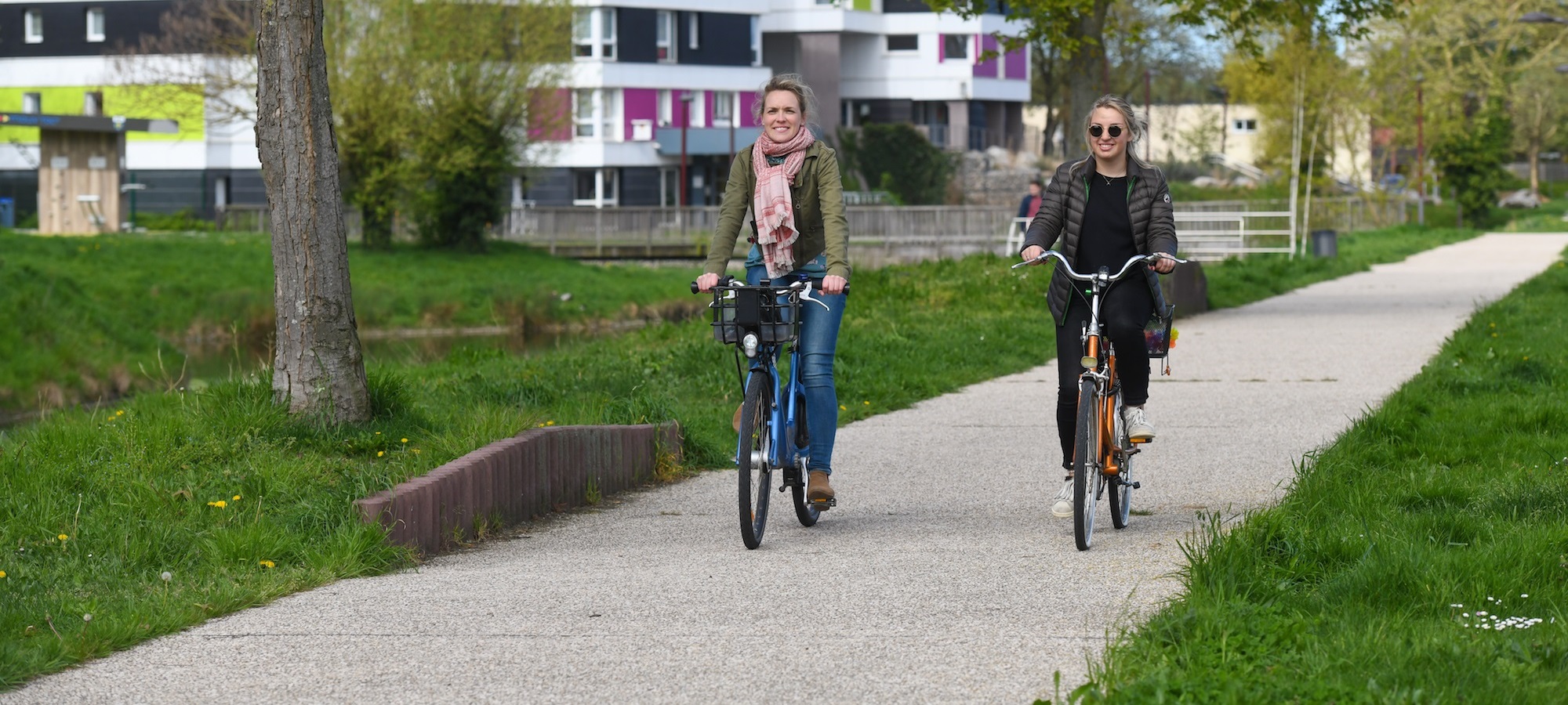 photo de deux jeunes femmes circulant sur une piste cyclable aménagée entre verdure et immeubles récents